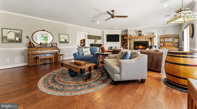 living room featuring crown molding, ceiling fan, wood-type flooring, and a stone fireplace