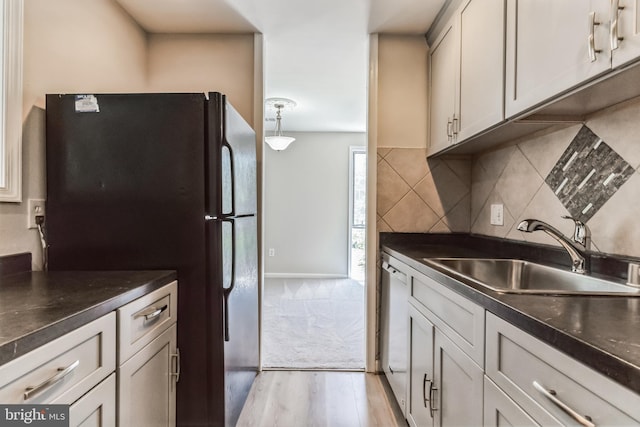 kitchen with sink, dishwasher, black fridge, decorative light fixtures, and light wood-type flooring