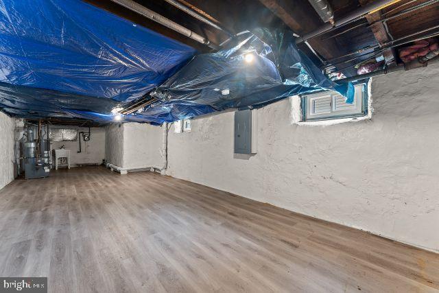 basement featuring gas water heater, wood-type flooring, electric panel, and a wealth of natural light