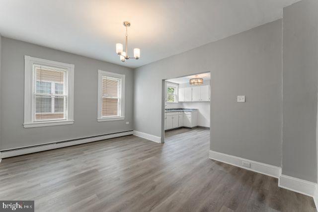 unfurnished dining area with baseboard heating, plenty of natural light, hardwood / wood-style floors, and a chandelier