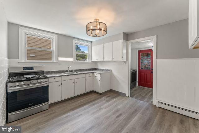 kitchen featuring sink, a baseboard radiator, a notable chandelier, stainless steel gas stove, and white cabinetry