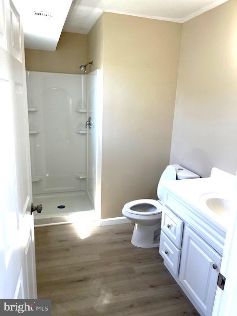 bathroom featuring wood-type flooring, toilet, vanity, and walk in shower