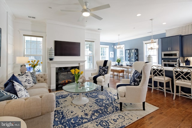 living room featuring dark hardwood / wood-style flooring, ceiling fan with notable chandelier, and ornamental molding