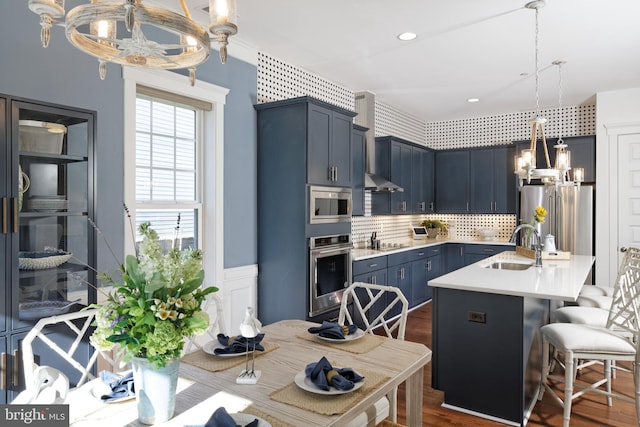 kitchen with backsplash, stainless steel appliances, sink, decorative light fixtures, and a center island with sink