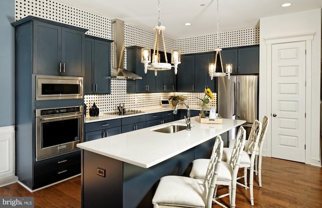 kitchen with a kitchen bar, appliances with stainless steel finishes, sink, a center island with sink, and hanging light fixtures