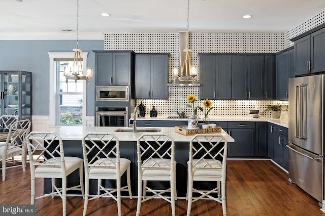 kitchen with a kitchen island with sink, sink, stainless steel appliances, and hanging light fixtures