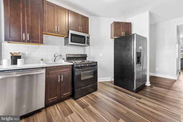 kitchen with decorative backsplash, dark brown cabinetry, stainless steel appliances, sink, and wood-type flooring