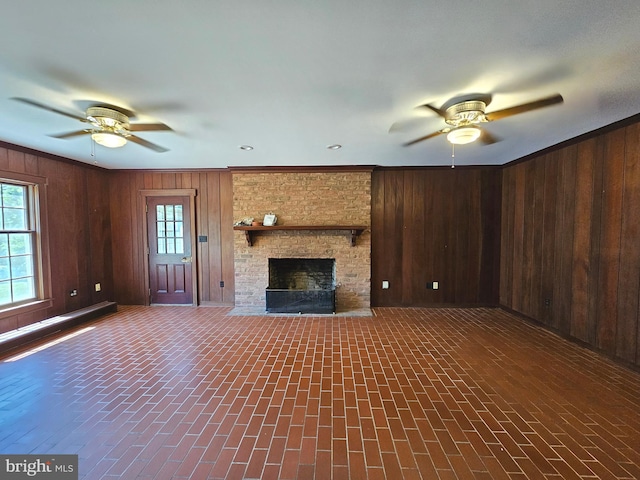 unfurnished living room with a brick fireplace, wooden walls, and ceiling fan