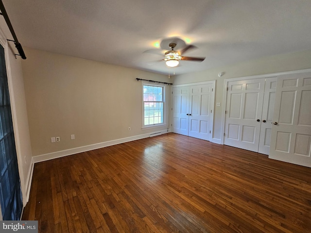 unfurnished bedroom with ceiling fan, dark hardwood / wood-style flooring, and two closets