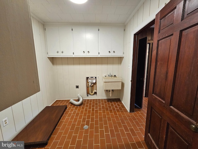 laundry area with sink, electric dryer hookup, cabinets, and wooden walls