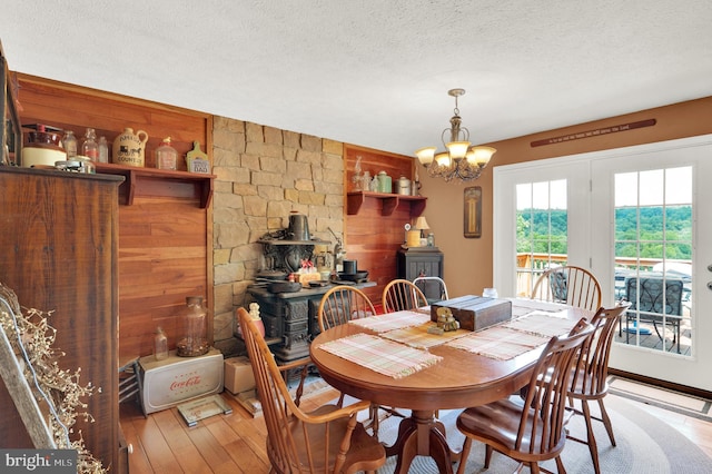 dining area with a textured ceiling, wood-type flooring, a notable chandelier, a wood stove, and wood walls