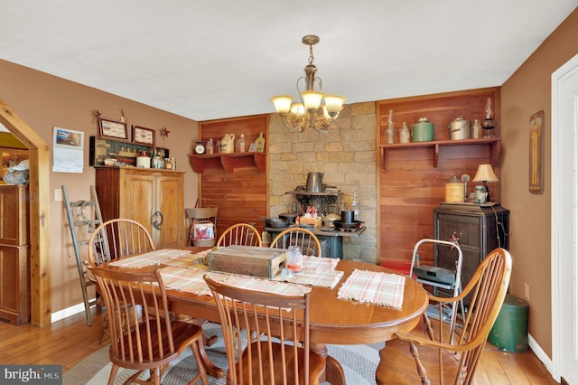 dining area with a wood stove, light hardwood / wood-style floors, and an inviting chandelier