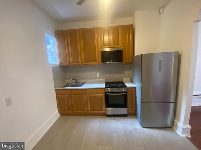 kitchen featuring ceiling fan, sink, light hardwood / wood-style flooring, backsplash, and appliances with stainless steel finishes