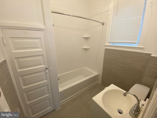 bathroom featuring washtub / shower combination, hardwood / wood-style floors, tile walls, and sink