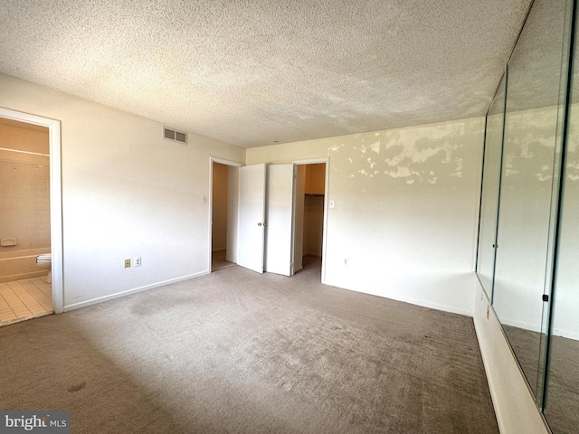 unfurnished bedroom with ensuite bath, a closet, carpet, and a textured ceiling