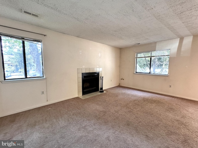 unfurnished living room with a textured ceiling, carpet flooring, a fireplace, and a wealth of natural light