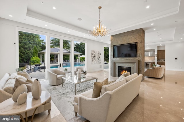 living room with a notable chandelier, a premium fireplace, and a tray ceiling