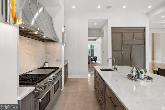 kitchen featuring built in appliances, light stone countertops, wall chimney range hood, and sink