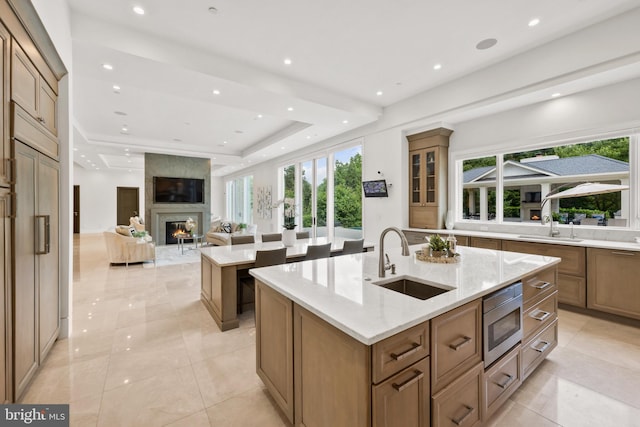 kitchen featuring a premium fireplace, a center island with sink, light stone countertops, and sink