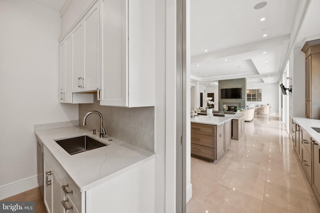 kitchen with white cabinetry, light stone countertops, sink, kitchen peninsula, and a tray ceiling