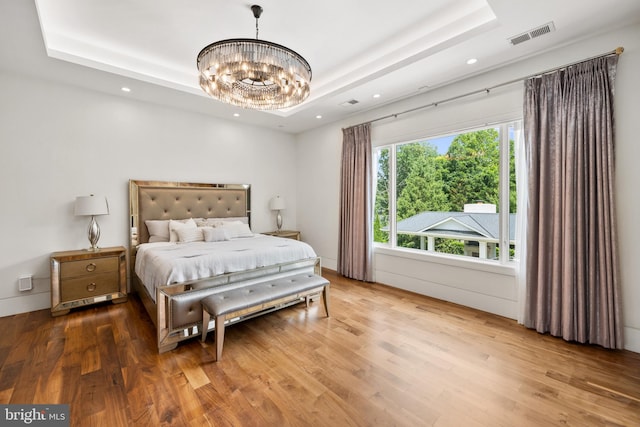 bedroom featuring hardwood / wood-style flooring, a raised ceiling, and a chandelier