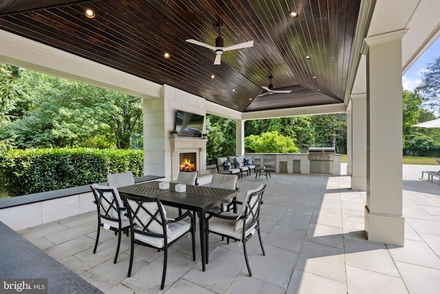 view of patio with an outdoor living space with a fireplace, ceiling fan, grilling area, and an outdoor kitchen