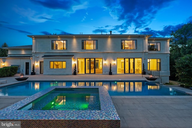 back house at dusk with a patio area and a swimming pool with hot tub