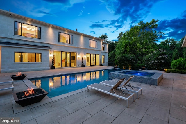 pool at dusk with an in ground hot tub, an outdoor fire pit, and a patio