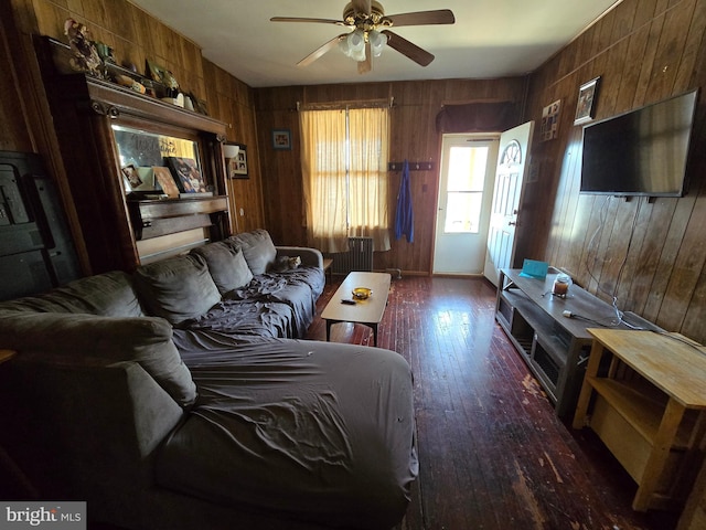 living room with ceiling fan, wood walls, and dark wood-type flooring