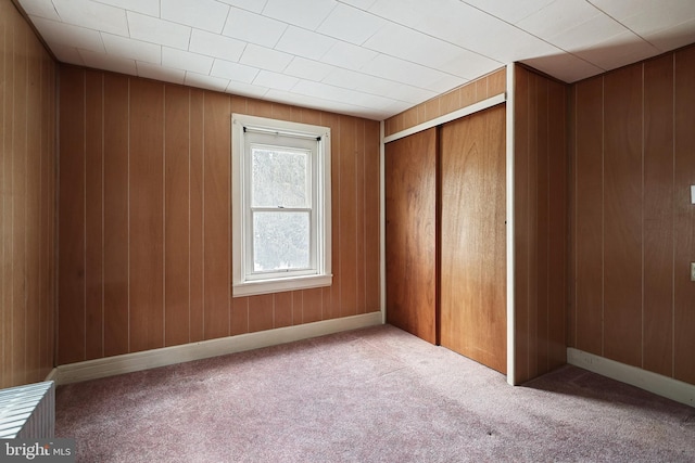 unfurnished bedroom featuring wood walls, a closet, and light colored carpet