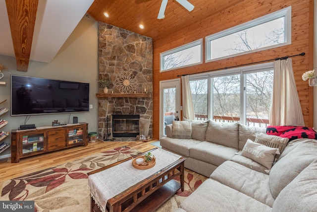 living room with ceiling fan, beam ceiling, hardwood / wood-style flooring, high vaulted ceiling, and a stone fireplace