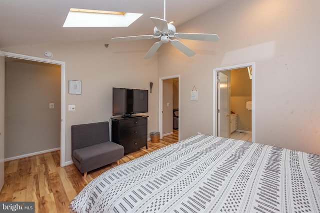 bedroom with ceiling fan, vaulted ceiling with skylight, ensuite bathroom, and light hardwood / wood-style floors