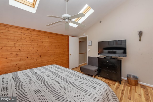 bedroom featuring ceiling fan, wood walls, light hardwood / wood-style floors, and vaulted ceiling