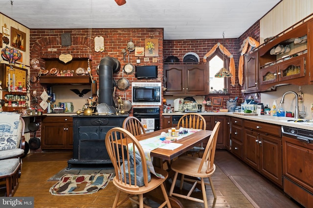 kitchen with a kitchen bar, brick wall, dark brown cabinetry, black appliances, and a wood stove