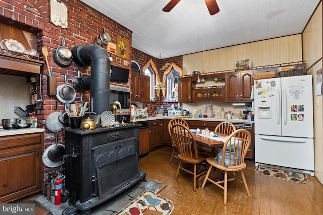 kitchen featuring a wood stove, sink, white fridge with ice dispenser, brick wall, and hardwood / wood-style flooring