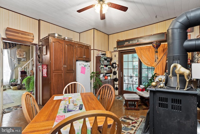 dining room with a wood stove, ceiling fan, wood-type flooring, wooden walls, and wood ceiling