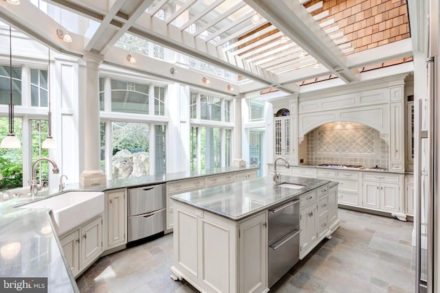 kitchen featuring backsplash, light stone counters, sink, and a kitchen island with sink