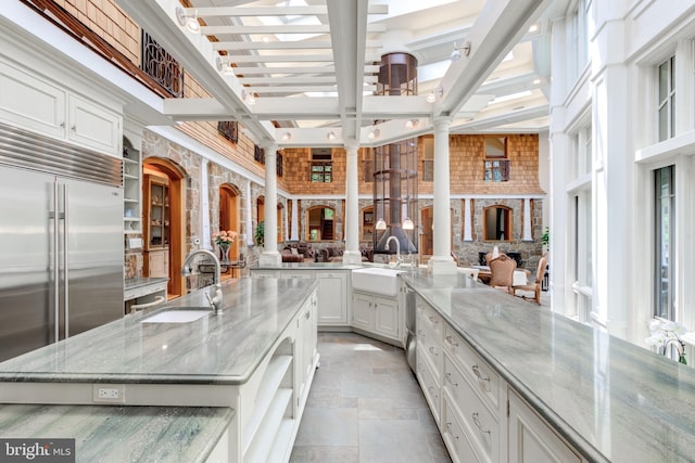 kitchen with light stone countertops, a large island with sink, built in fridge, and sink