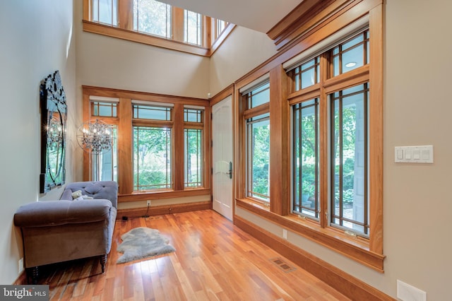 living area with plenty of natural light, light hardwood / wood-style floors, a high ceiling, and a notable chandelier