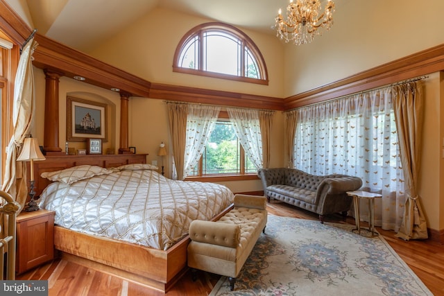 bedroom featuring a chandelier, hardwood / wood-style floors, a towering ceiling, and decorative columns