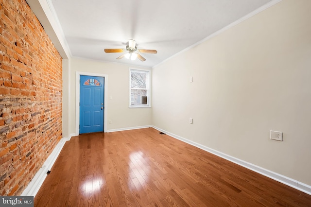 unfurnished room with ceiling fan, hardwood / wood-style floors, brick wall, and ornamental molding