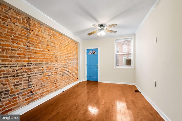 unfurnished room featuring hardwood / wood-style flooring, ceiling fan, ornamental molding, and brick wall