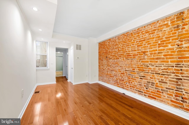 spare room with light hardwood / wood-style floors and brick wall