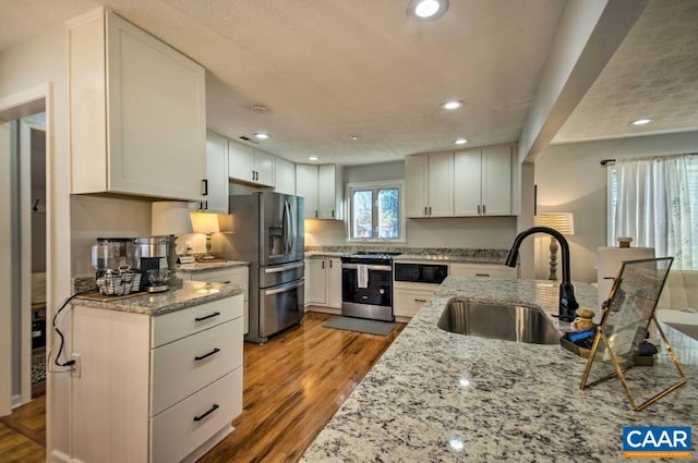 kitchen featuring light stone countertops, stainless steel appliances, sink, light hardwood / wood-style floors, and white cabinetry