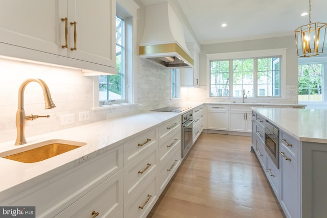 kitchen featuring premium range hood, white cabinets, sink, decorative backsplash, and light stone counters