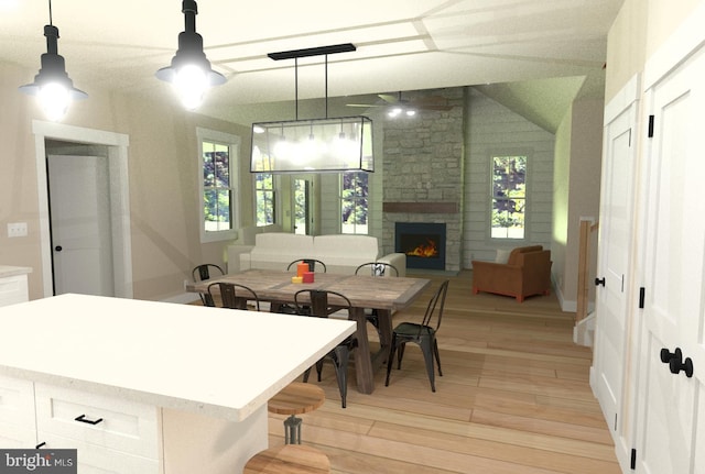 dining space featuring a fireplace, a healthy amount of sunlight, vaulted ceiling, and light hardwood / wood-style floors