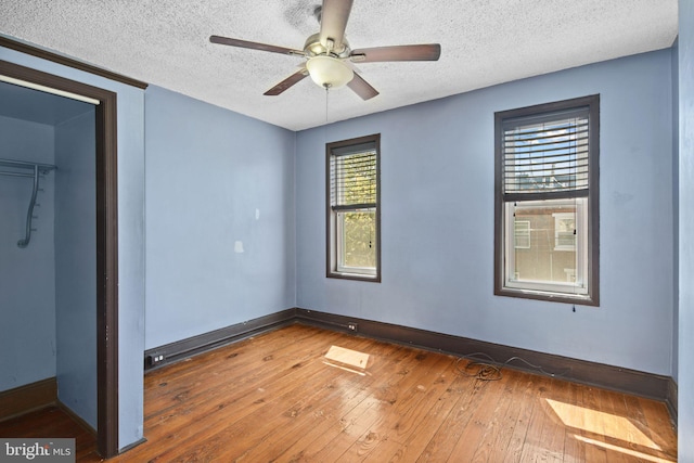 unfurnished bedroom featuring hardwood / wood-style floors, ceiling fan, a spacious closet, and a textured ceiling