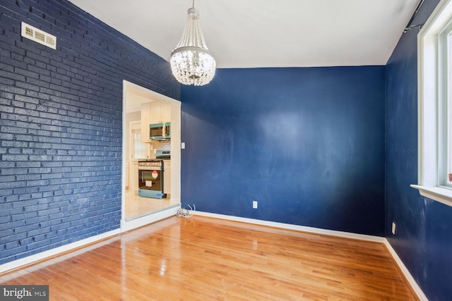 empty room with hardwood / wood-style flooring, brick wall, and an inviting chandelier