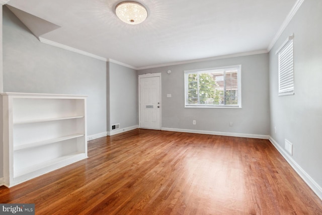 unfurnished room with hardwood / wood-style flooring, built in shelves, and crown molding