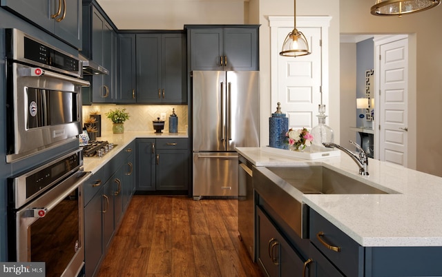 kitchen with appliances with stainless steel finishes, backsplash, light stone counters, dark wood-type flooring, and pendant lighting